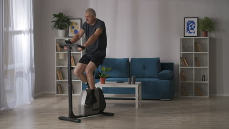 El-Deportista-Está-Entrenando-En-Bicicleta-Estática-En-Ejercicios-Cardiovasculares-En-Casa-Para-Mantener-Una-Buena-Condición-Física-En-El-Fitness-Y-El-Deporte-De-Mediana-Edad.